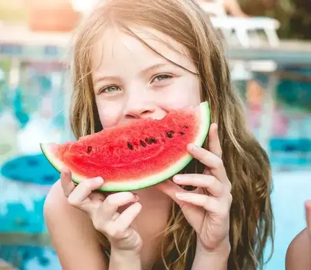 Mädchen geniesst eine Melone im Sommer am Gartenpool