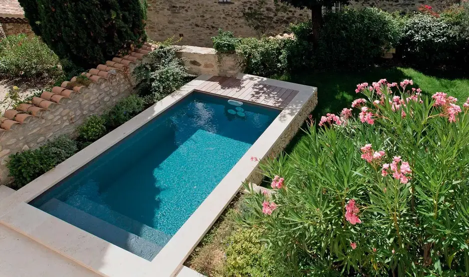 Rechteckiger Pool mit Holzterrasse in bepflanztem Garten
