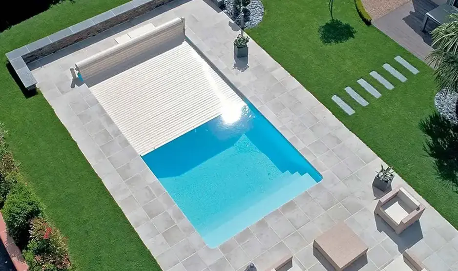 Pool im Garten mit grauen Terrassenplatten eingefasst und elektrischer Poolabdeckung.