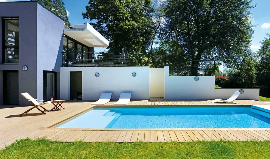 Eigenheim mit großen Pool, Holzterrasse und Sonnenliegen im Garten.